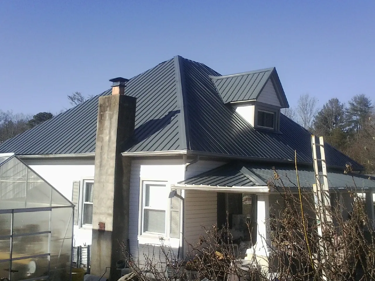 Dark blue standing seam metal roof on a white farmhouse with dormer — Slate & Tile Roof Repair by Roofing Brothers in Weidman
