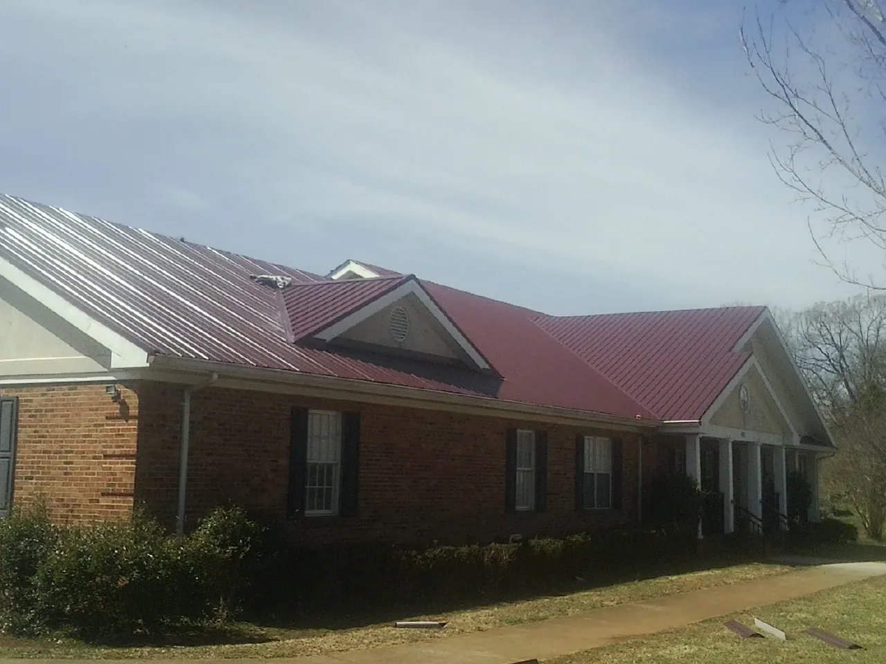 Red metal roof with gabled entries on a long brick building, from a Hail Damage Roof Repair job in Weidman