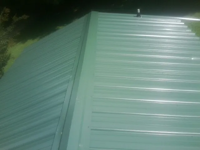 New green metal panels meeting at the ridge of a roof — Flat Roof Repair work by our crew in Weidman