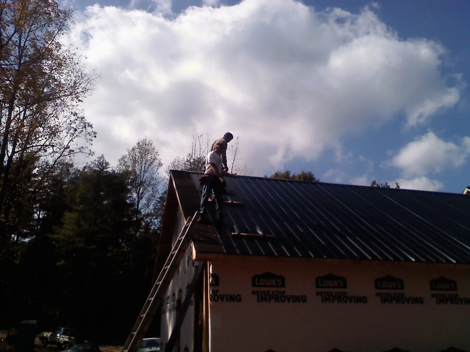 Roofer fastening dark metal panels high against a cloudy sky, from a Roof Inspection job in Weidman